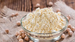 Chickpea flour in a glass bowl with some chickpeas next to it