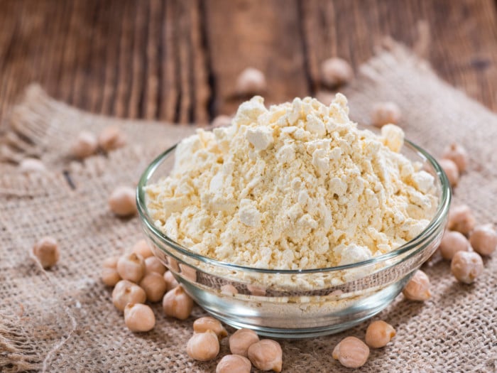 Chickpea flour in a glass bowl with some chickpeas next to it