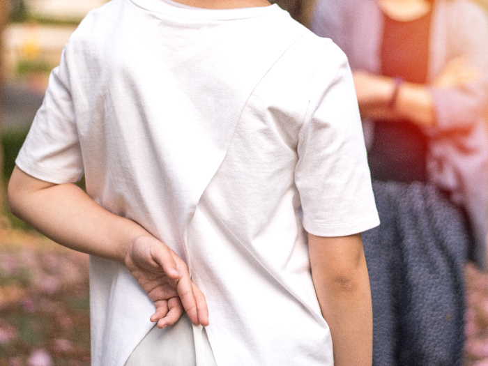 A child crossing fingers behind their back while facing an adult