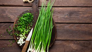 Chopped and full chives on a wooden cutting board
