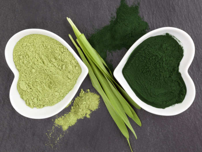 Two heart-shaped bowls, one containing dark green powder and the other containing light green powder with husks placed in between on a dark slate background.