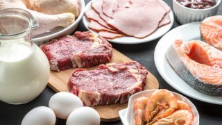 Flatline view of fried rice topped with sliced avocado and a fried egg, placed alongside a glass of tea on a wooden surface.