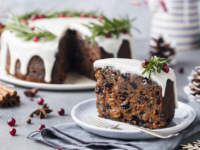 A close-up picture of Christmas fruit cake, pudding on white plate against a background of christmas decoration.