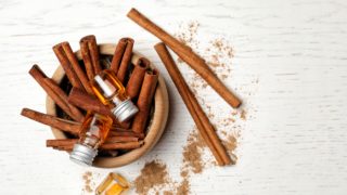 A bowl of cinnamon sticks with a bottle of cinnamon oil on a white background