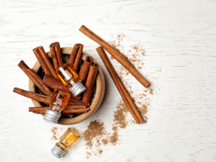 A bowl of cinnamon sticks with a bottle of cinnamon oil on a white background