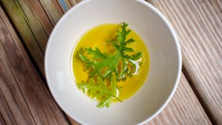 A white bowl of citronella oil and fresh citronella leaves placed on the oil