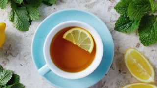 A white and blue cup and saucer filled with tea and a lemon slice in it.