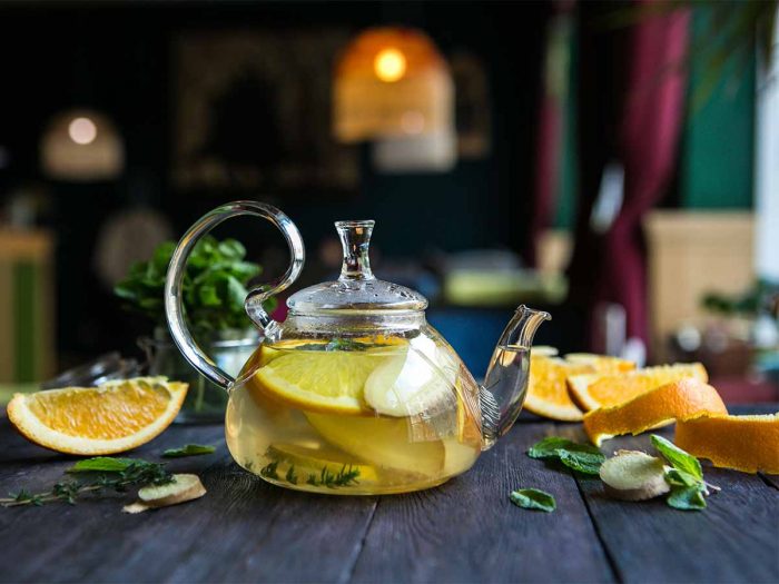 A transparent kettle filled with lemon tea and surrounded by citrus fruits and mint leaves