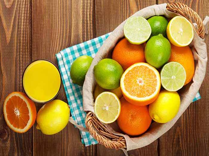 Basket of citrus fruits with a couple of fruits and a glass of juice alongside on a wooden surface