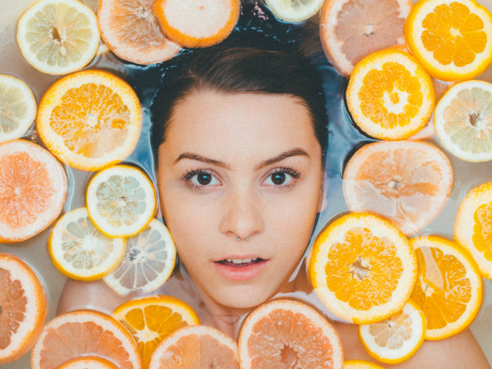 Close up of a woman's face with body immersed in water, surrounded by citrus slices