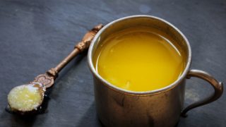 A traditional brass container and a spoon of clarified butter or ghee on a dark background