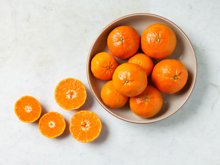 A bowl of fresh whole and halved clementines on a white background