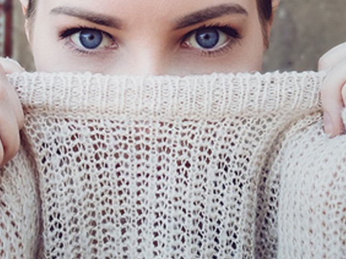 A girl peeking at the camera from behind the sweater