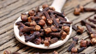 A close up of wooden spoon filled with dried cloves
