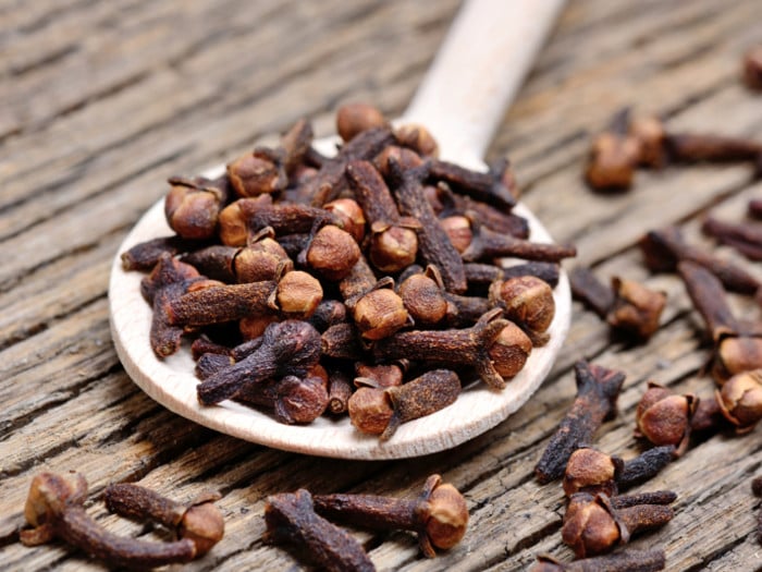 A close up of wooden spoon filled with dried cloves