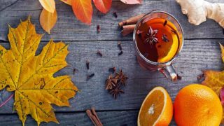 Oranges and cloves on a black counter with autumn leaves next to a clove tea cup