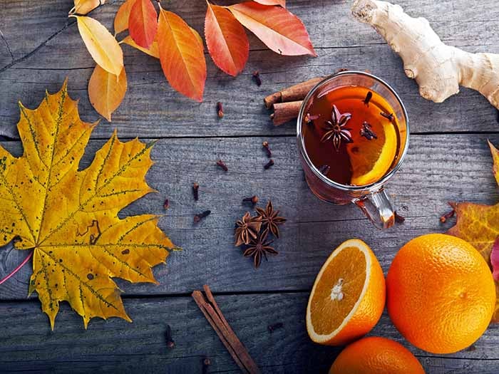 Oranges and cloves on a black counter with autumn leaves next to a clove tea cup