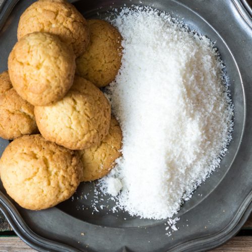 Coconut cookies kept next to coconut flour, on a steel plate.