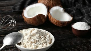 A bowl full of coconut flour kept next to coconuts atop a black platform