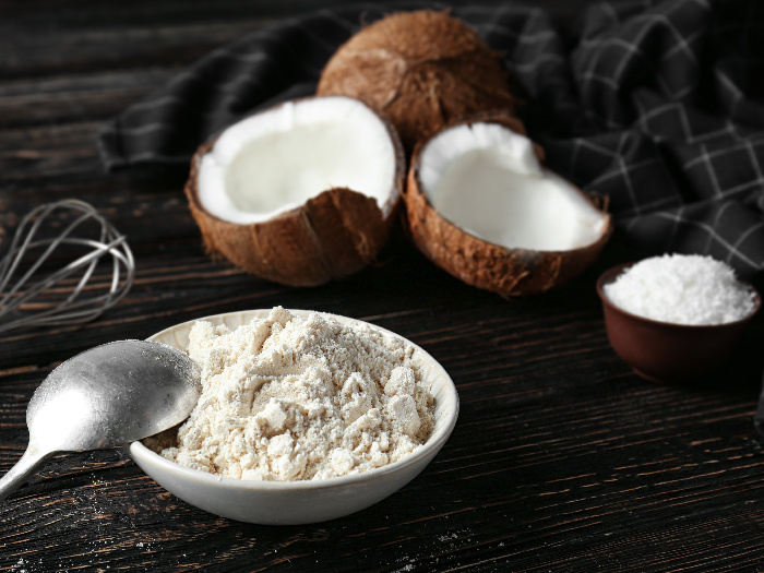 A bowl full of coconut flour kept next to coconuts atop a black platform