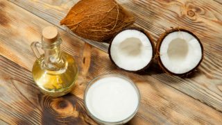 A bottle of coconut oil and a few coconuts on a wooden floor