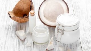 An image showing coconut face wash, oil & cream kept next to a coconut against a white background
