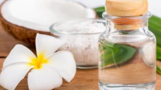 A bottle of coconut oil with a small bowl of coconut cream and a halved coconut with white flower on a wooden table