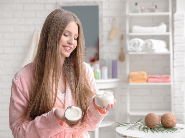 A woman with long hair in the bathroom holding a coconut and a hair mask bottle