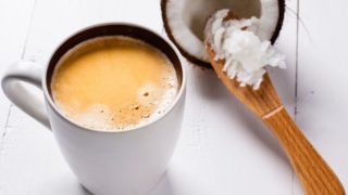 A cup of coffee next to halved coconut scooped with a butter knife