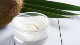 A lotion made from coconut oil in a bowl, with a coconut in the background
