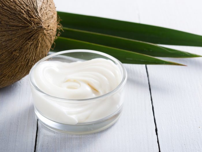 A lotion made from coconut oil in a bowl, with a coconut in the background