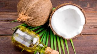 whole coconut and a coconut half placed next to oil bottle on a wooden surface.