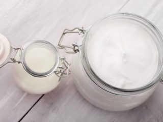 coconutoilsunscreen Coconut oil lotion in a large glass jar, next to coconut oil in a small jar