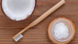 Flatlay view of a wood toothbrush placed in between a bowl of coconut cream and a coconut half.