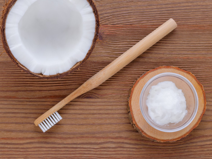 Flatlay view of a wood toothbrush placed in between a bowl of coconut cream and a coconut half.