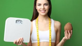 A woman with a fitness tape, happy with her weight, holding a coconut and scale on a green background