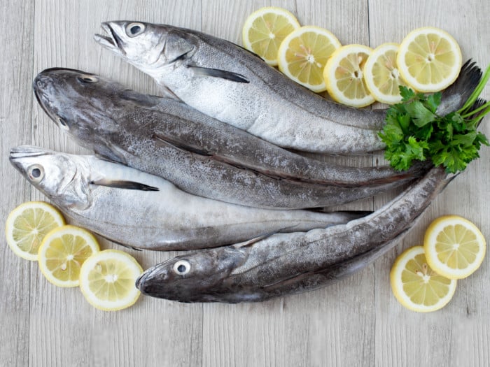 Four cod fishes on a wooden table with lemon and herbs