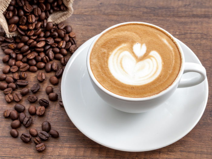 A cup of fresh cappucino beside a bag of coffee beans on a wood surface
