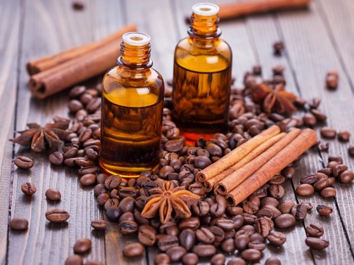 Two small bottles of coffee essential oil surrounded by coffee beans and cinnamon sticks and placed atop a wooden platform