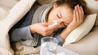 A young woman with a blanket lying on a couch suffering from cold and flu