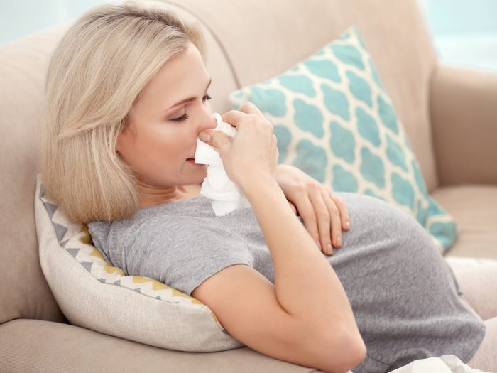 A pregnant woman wiping her nose in a napkin