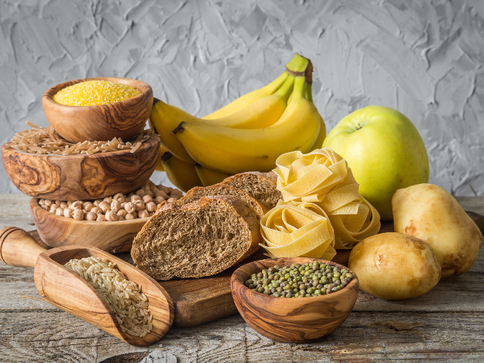 Brown bread, pasta, bananas, rice, wheat, and beans in wooden bowls on a wooden table