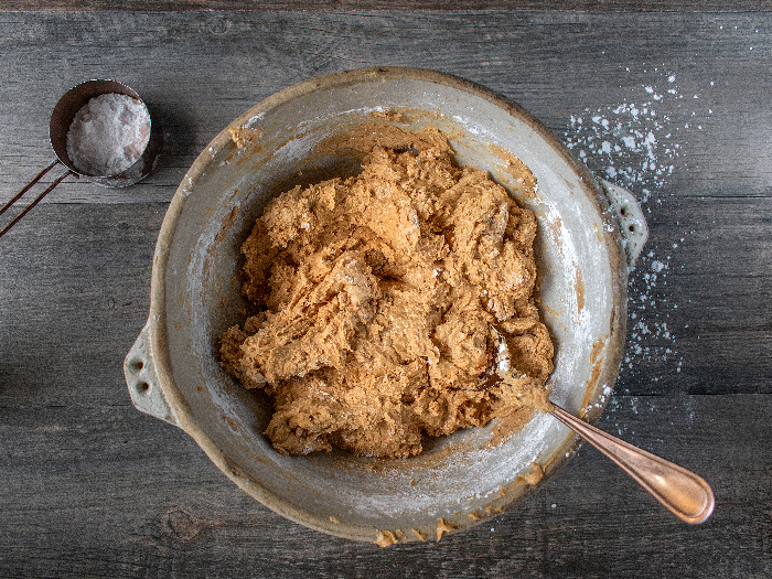 Cookie dough in a large bowl with a spoon next to a spoon of flour on a wooden table