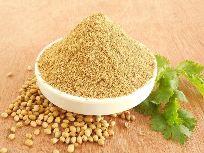 A close up shot of coriander powder and coriander seeds kept atop a wooden platform