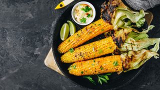 A top view picture of roasted or grilled sweet corn cobs with garlic butter and lime placed on dark gray stone background