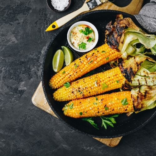 A top view picture of roasted or grilled sweet corn cobs with garlic butter and lime placed on dark gray stone background