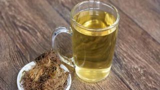 A cup of corn silk tea kept beside a bunch of corn silk on top of a wooden platform