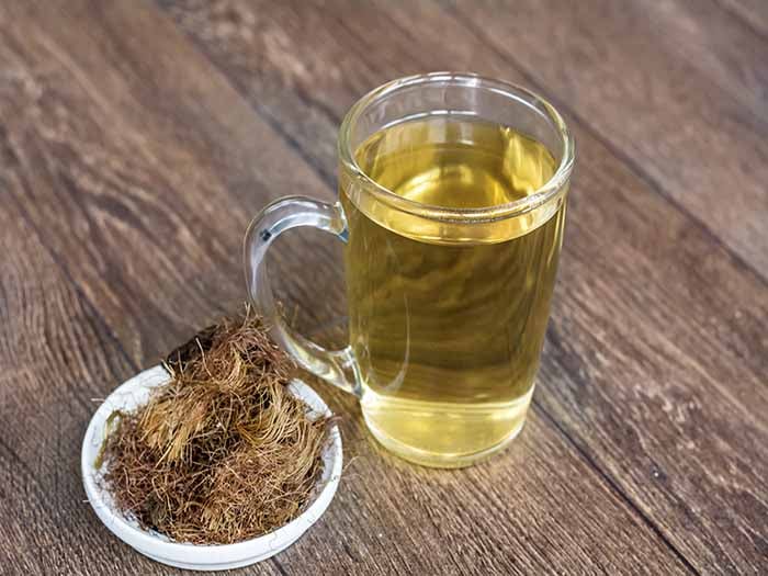 A cup of corn silk tea kept beside a bunch of corn silk on top of a wooden platform