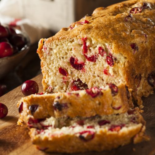 Cranberry bread loaf with a couple of slices next to cranberries on a counter