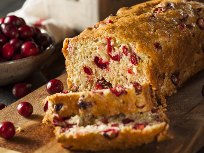 Cranberry bread loaf with a couple of slices next to cranberries on a counter